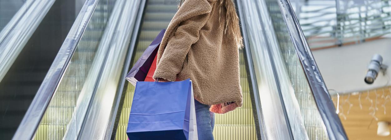 mulher segurando sacos de compras e subindo escadas rolantes