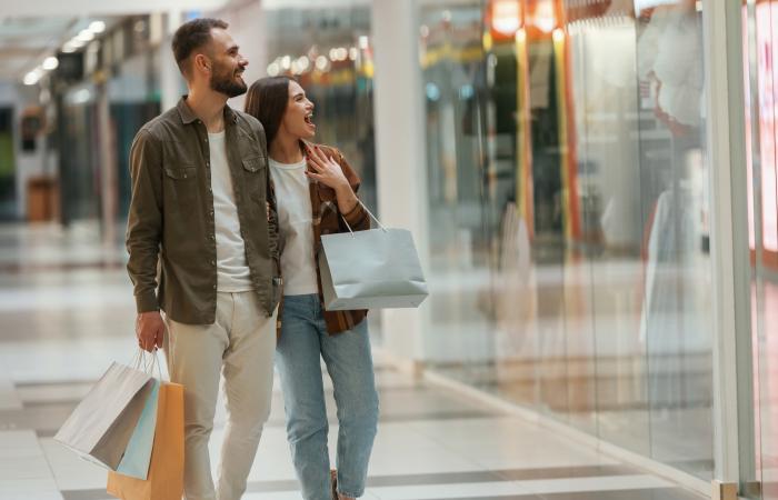 casal com sacos a olhar montra dentro de centro comercial